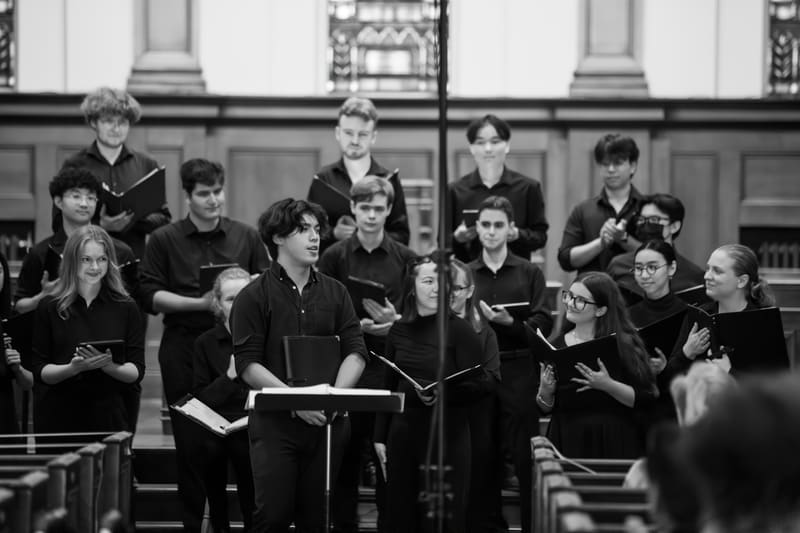 Black-and-white photo of Matthew Menard at a music stand in front of a youth choir