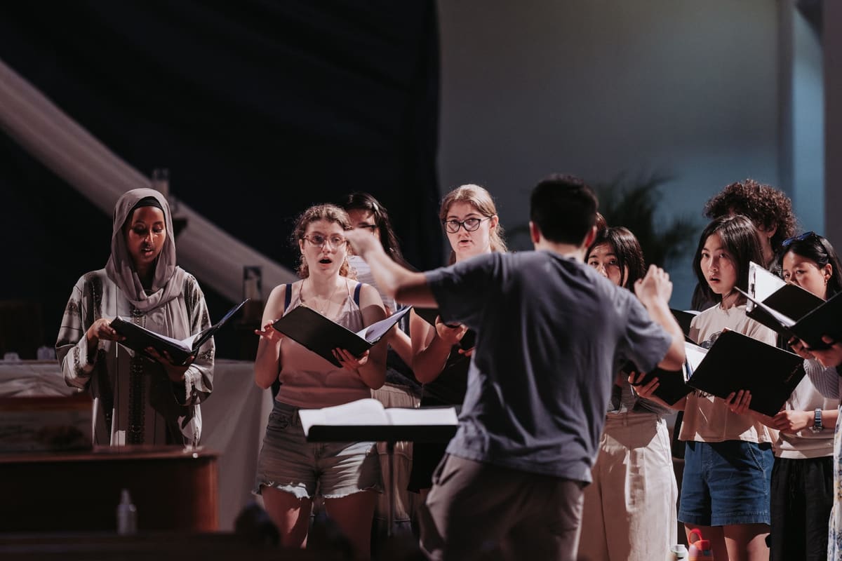 Matthew Menard, seen from behind, conducting a choir holding black folders