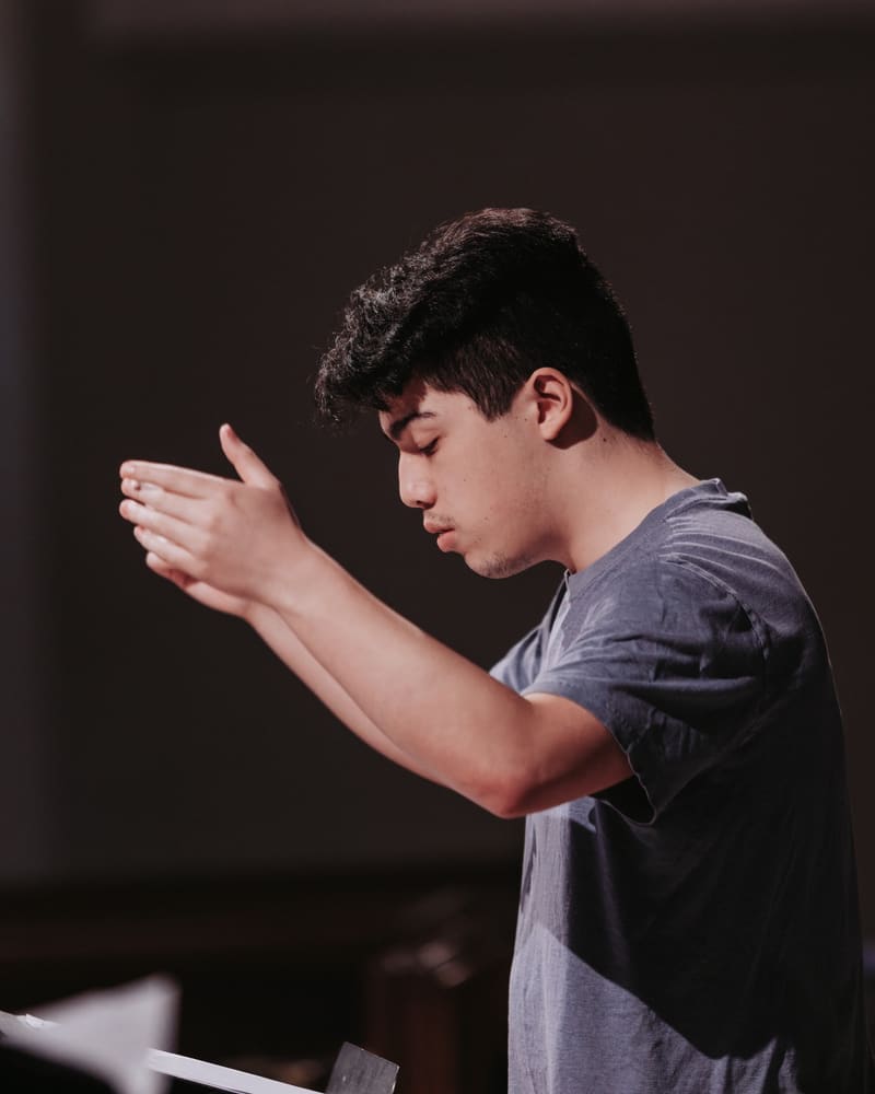 Matthew Menard in profile, conducting with both hands raised