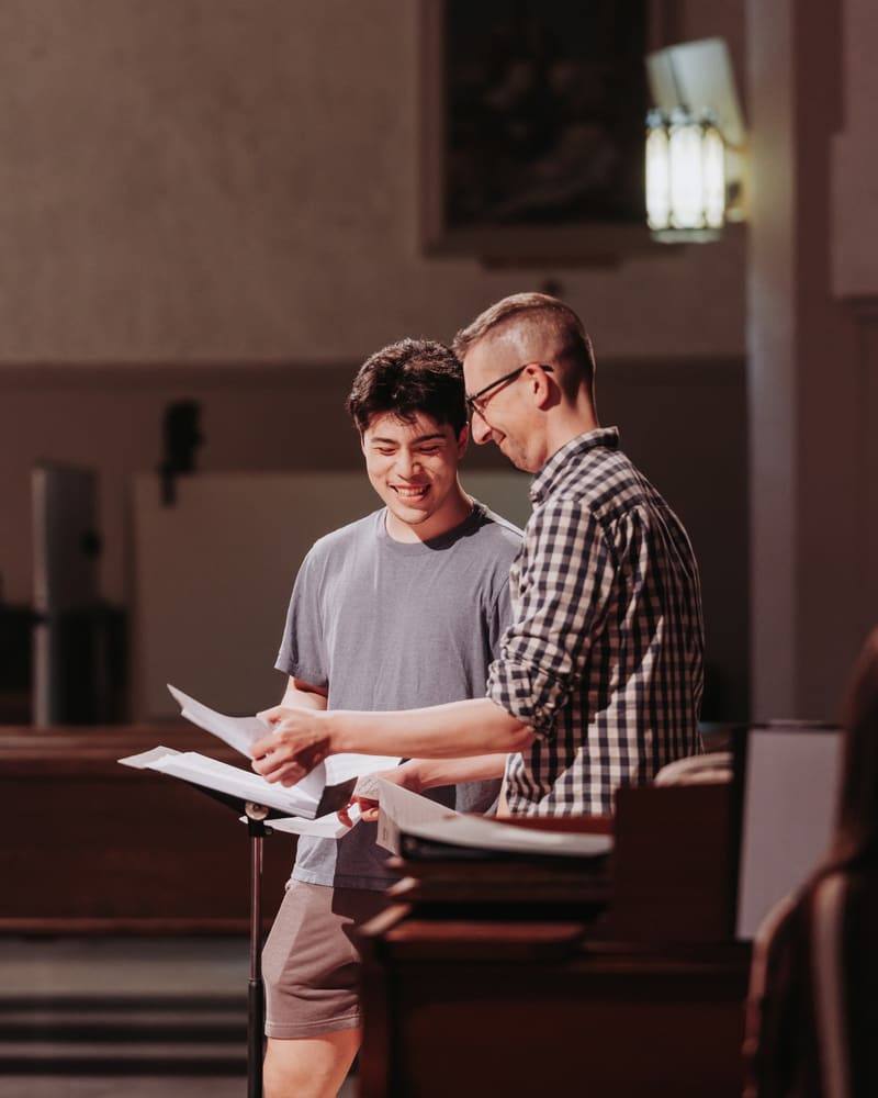 Matthew Menard smiling with a colleague over sheet music at a music stand in a church